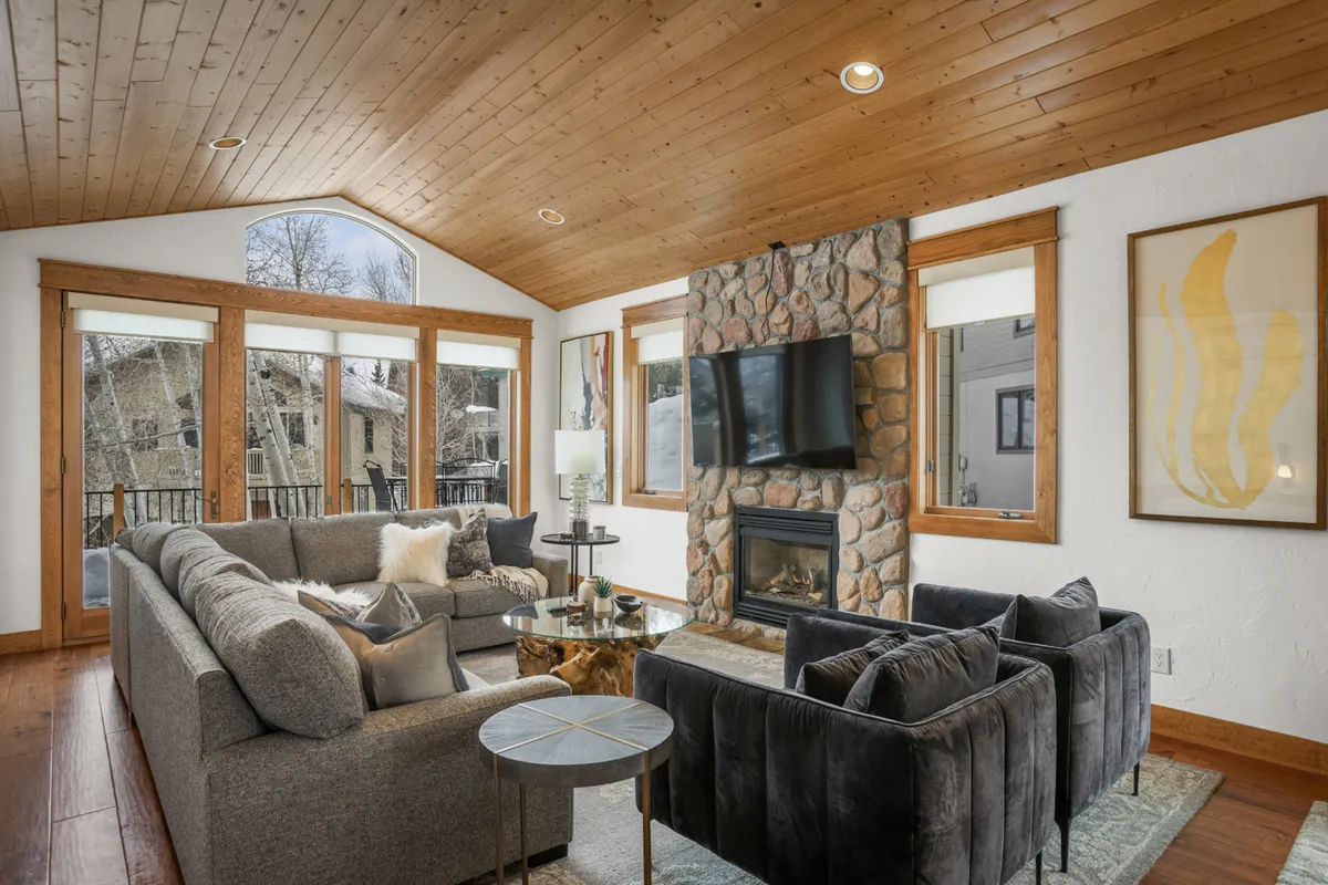 An inviting living area with a stone fireplace, large windows offering views of nature, comfortable seating, and tasteful wall art, exuding warmth and relaxation.