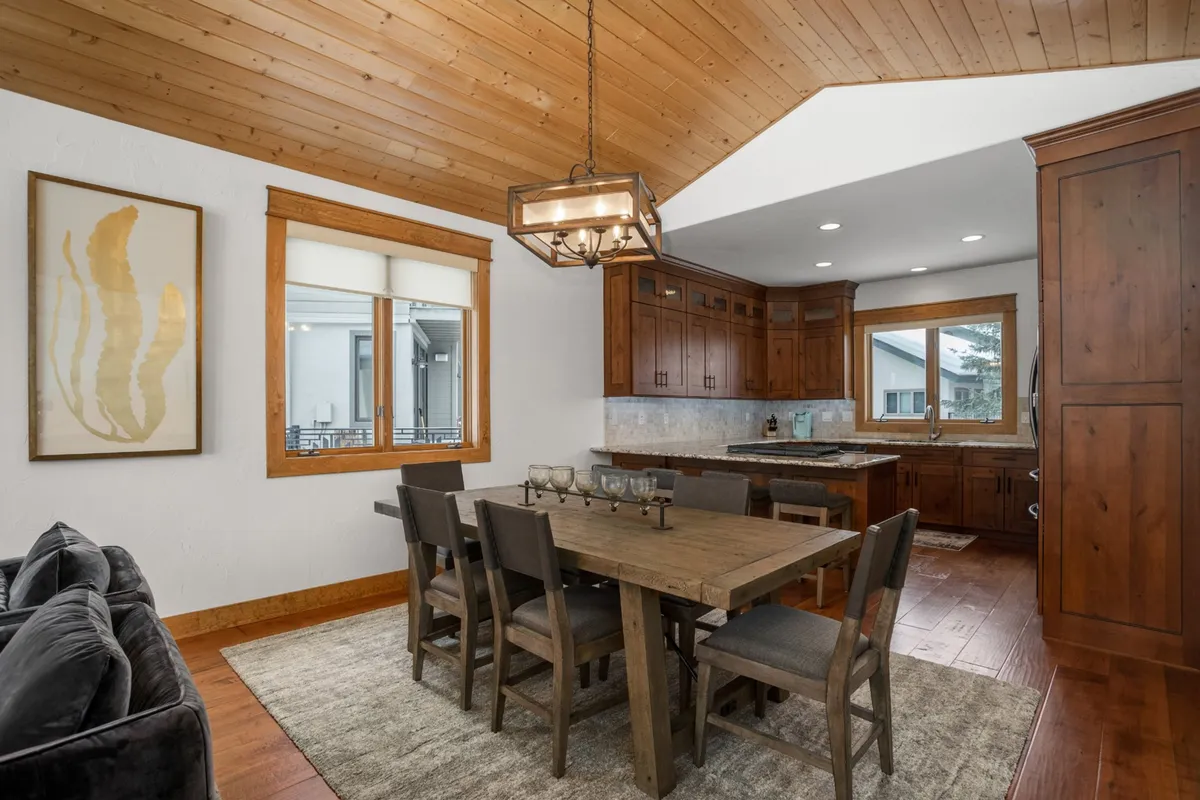 The dining area features a wooden table surrounded by comfortable seating, complemented by warm cabinetry and artistic wall décor. The setting is arranged for a shared meal, evoking a sense of togetherness and celebration.