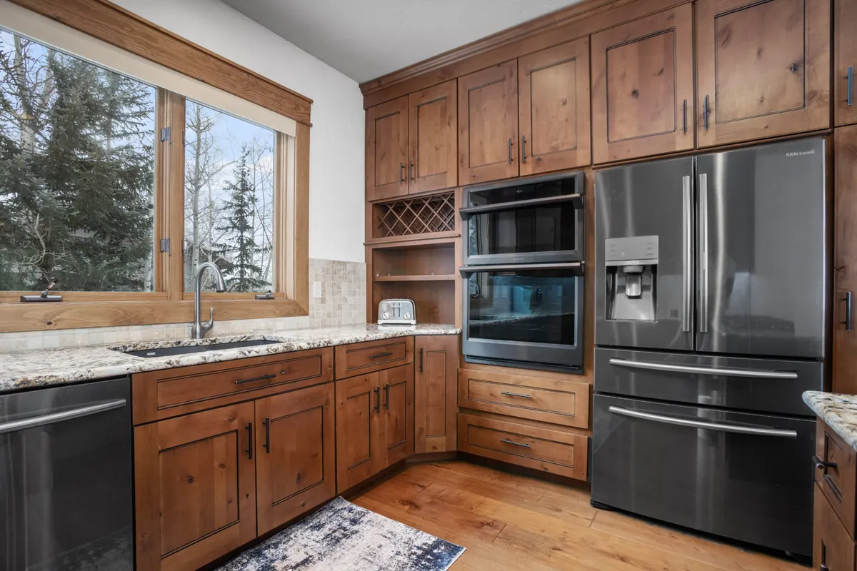 This image showcases a spacious, modern kitchen with a granite countertop, high-end modern appliances, and warm wood cabinetry. A large window brings in natural light, making the space feel bright and inviting—the perfect environment for preparing meals and entertaining guests.