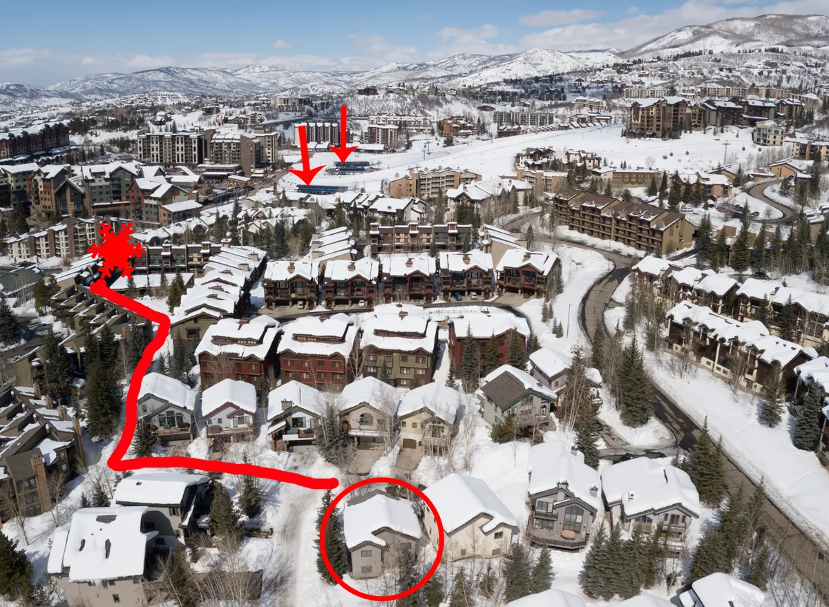 A sweeping view of snow-dusted rooftops, winding roads, and a distant mountain range, framed by trees. The image captures the broader Steamboat Resort environment, conveying both the excitement of outdoor adventure and the peacefulness of a mountain community.