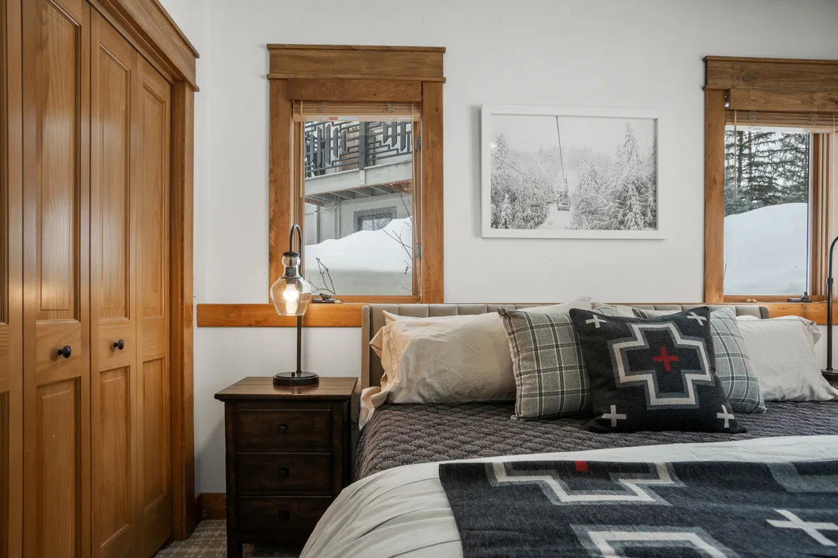 A serene bedroom with a plush bed, nightstand, large windows framing mountain views, and tasteful artwork. The space radiates peace and privacy, offering a perfect sanctuary after a day of adventure.
