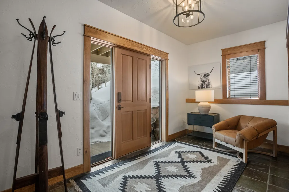 A cozy entryway featuring a welcoming front door, a comfortable armchair, a stylish rug, a lamp, and wall art. The space is softly lit and immediately gives a sense of home and warmth, perfect for first impressions as you enter.