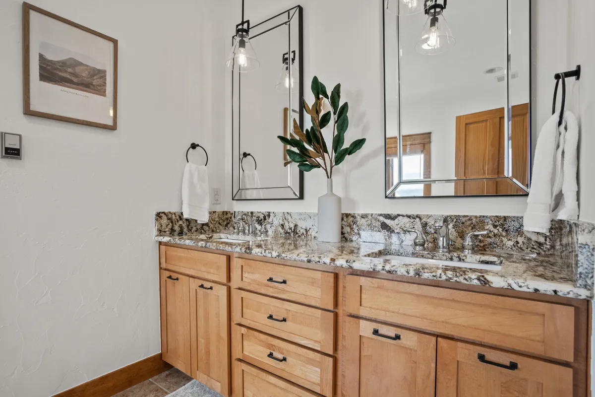 A serene bathroom featuring a double sink vanity, framed mirrors, and a decorative plant. The soft lighting and spacious layout create an inviting, spa-like ambiance ideal for morning routines or evening relaxation.