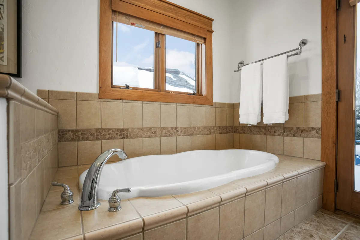A tranquil bathroom scene with a large bathtub beside windows, fresh towels, and serene views to the outdoors. The space exudes spa-like luxury and calm, ideal for unwinding after a long day.