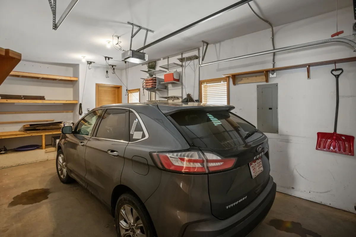 A practical and organized heated garage with a gray car parked, shelves, overhead storage, and windows that let in daylight. The setup is clean, functional, and ready for storing gear after mountain adventures.