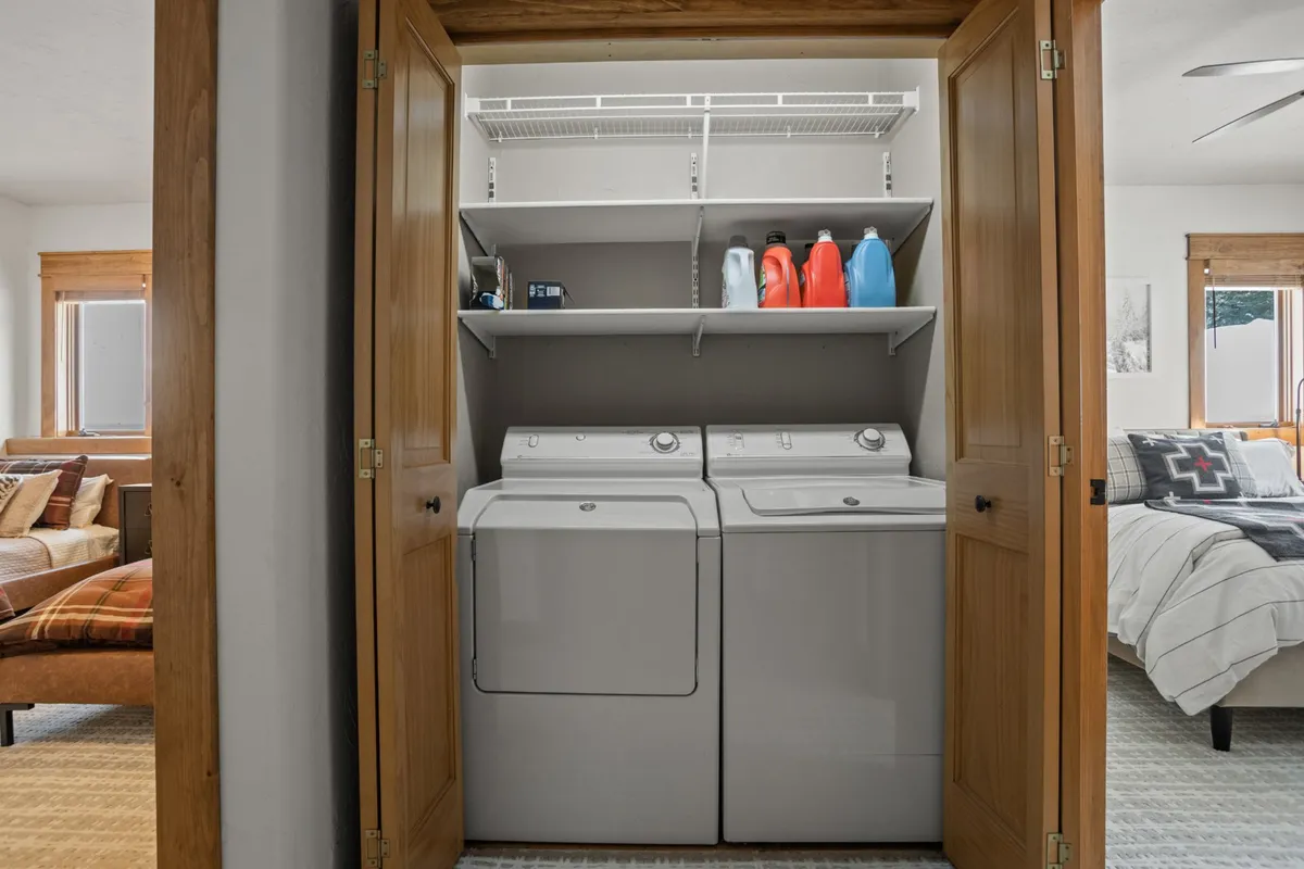 A practical laundry space featuring a stacked washer and dryer, shelves with detergent bottles, and wooden doors, all set in a tidy, well-organized area.