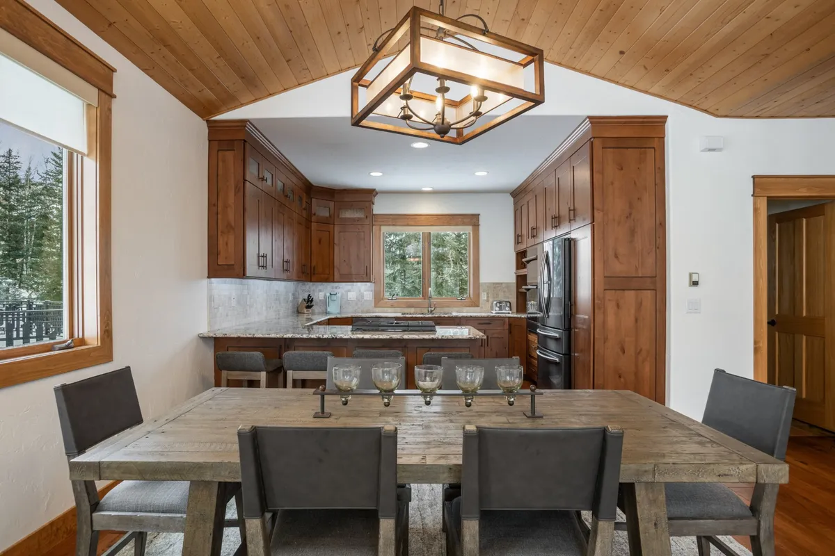A bright dining area with a large table sits beside a window offering mountain views. The space is complemented by wooden cabinetry, creating a warm and communal setting ideal for holiday celebrations or casual meals with loved ones.