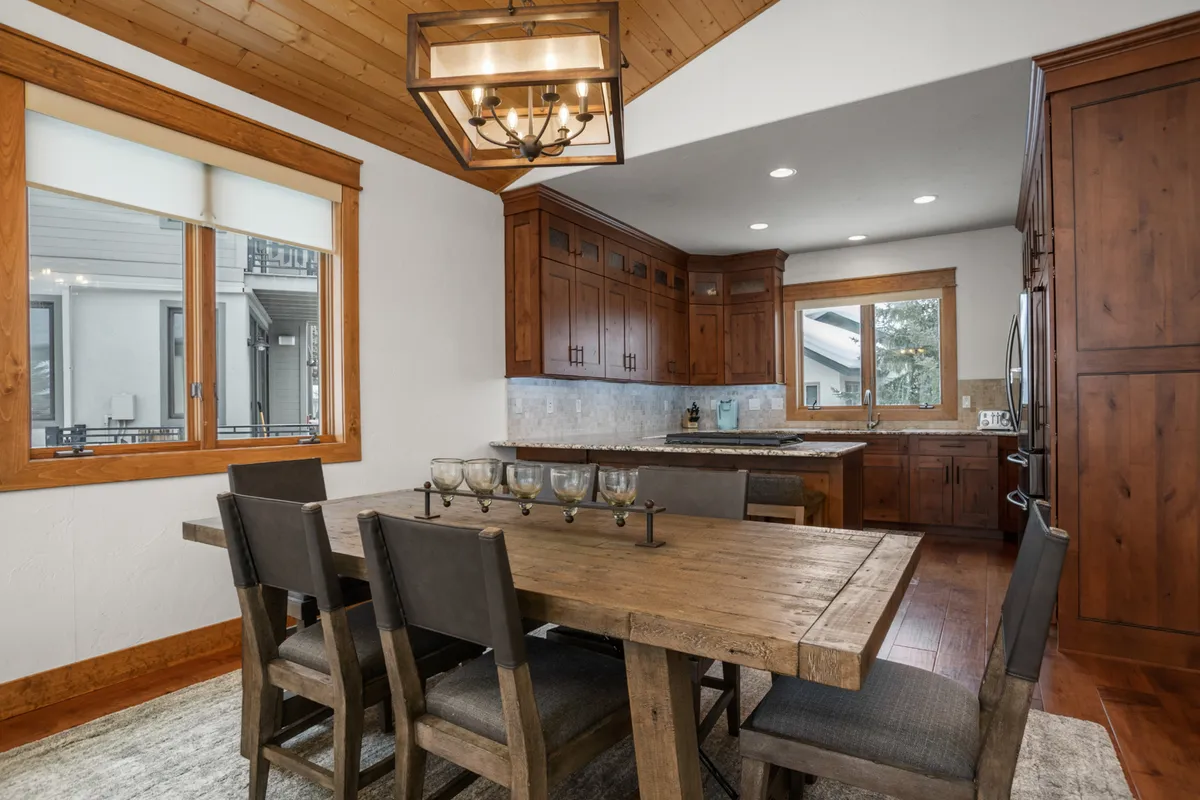 A warm, open-concept dining space featuring a wooden dining table, elegant kitchen cabinetry, a chandelier, and expansive windows that let in natural light. The scene suggests intimate family dinners or festive gatherings in a tastefully furnished setting.